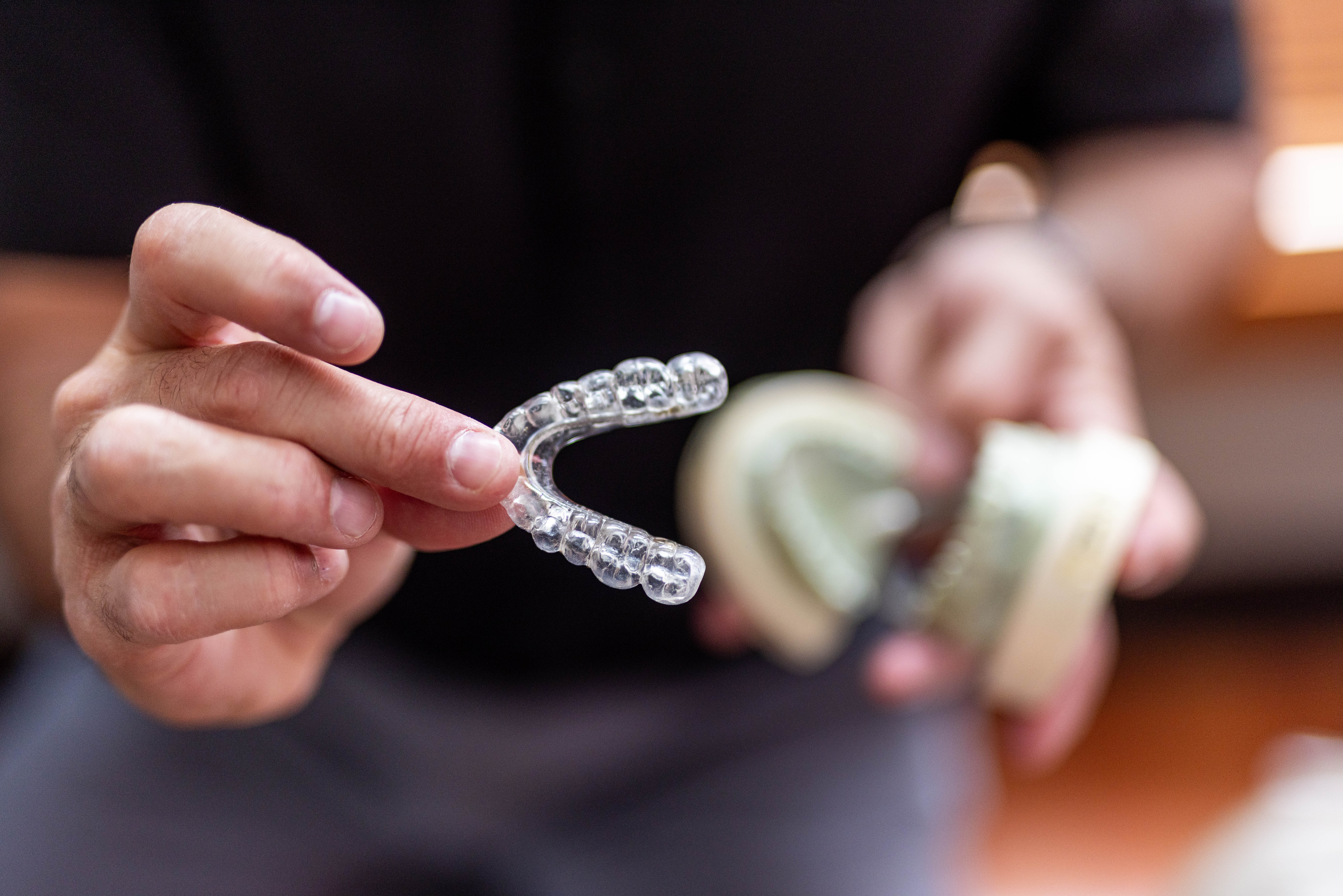 RAD-0359 - Rochester Advanced Dentistry - Rochester Advanced Dentistry Close-up of hands holding a clear dental aligner against a dark background