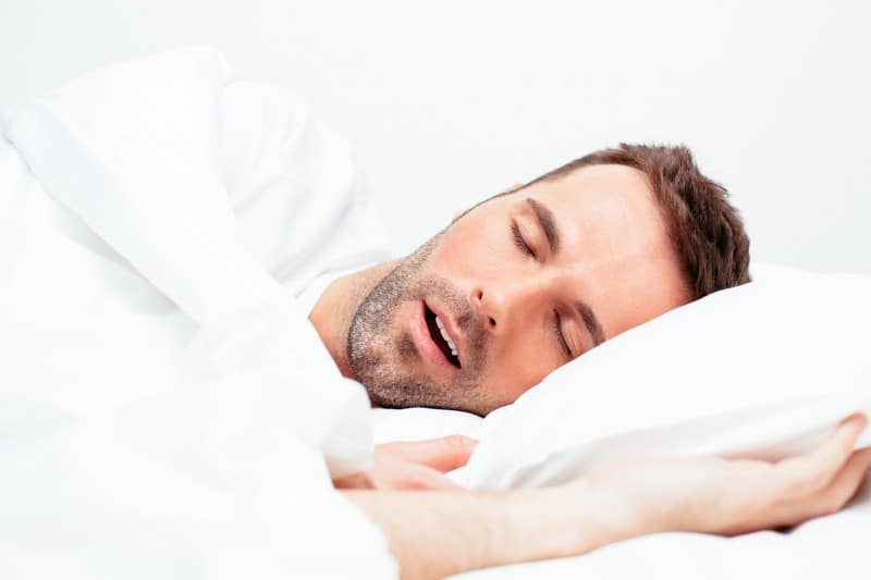 Man laying on his side, snoring. His sleep apnea could be related to a number of health issues including acid reflux or diabetes.