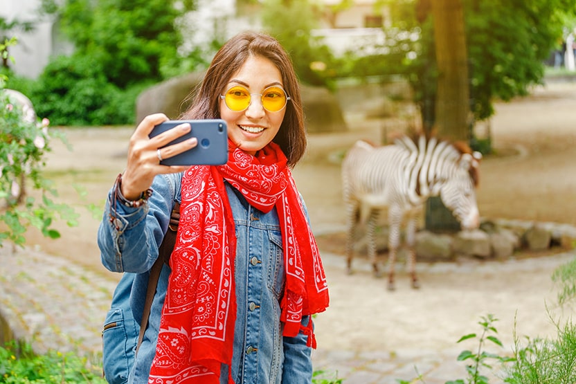 Young woman safely taking a selfie with zebra in the background