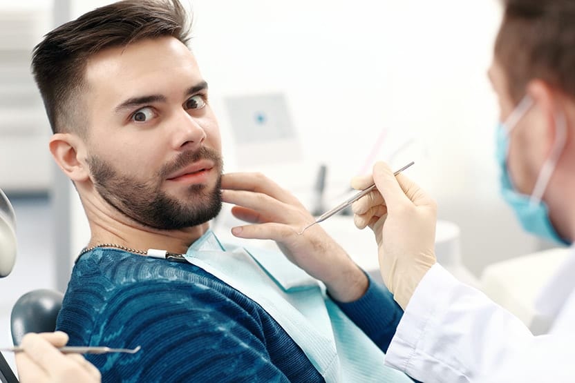A young man sitting in a dental chair, scared about seeing his dentist for a cleaning. If you have anxiety over seeing a cosmetic dentist concern sedation dentistry with Dr. Haddad and Dr. Doolin of Rochester Advanced Dentistry. 
