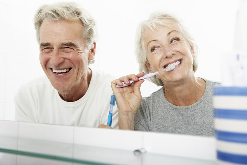 A senior couple brushing their teeth in the bathroom. Brushing is just one of the preventive dentistry tips to make sure you keep your smile looking great!