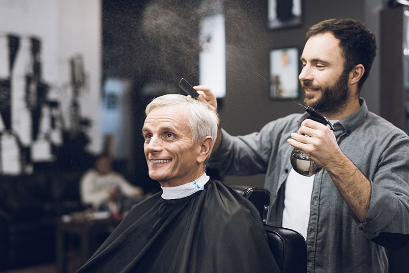 a barber sprays water into an older male's hair as he gets a haircut