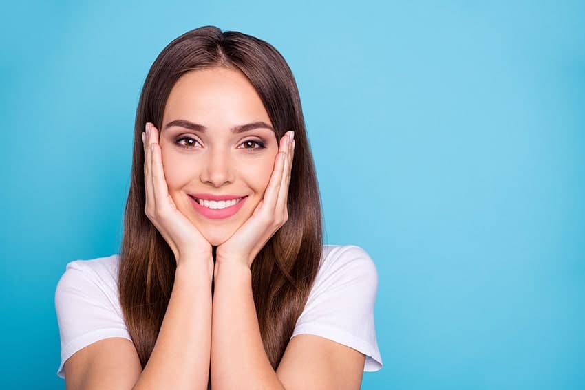 Pretty woman shows off her smile with her hands resting on her cheeks