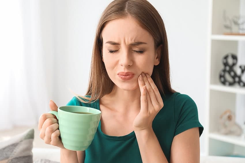 Young woman with sensitive teeth sips her coffee in pain