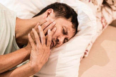 older Asian man lays in bed with jaw pain