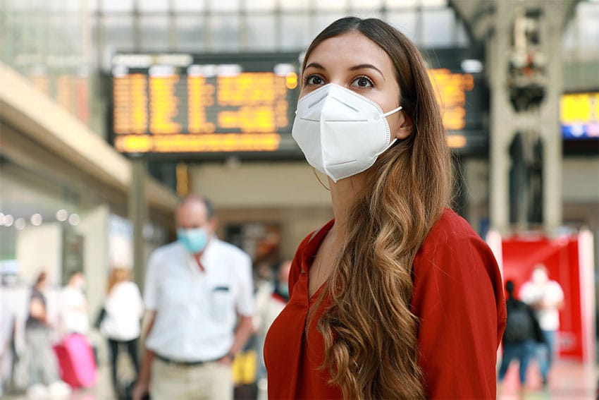 woman with attractive eyes and COVID-19 mask stands in a busy airport
