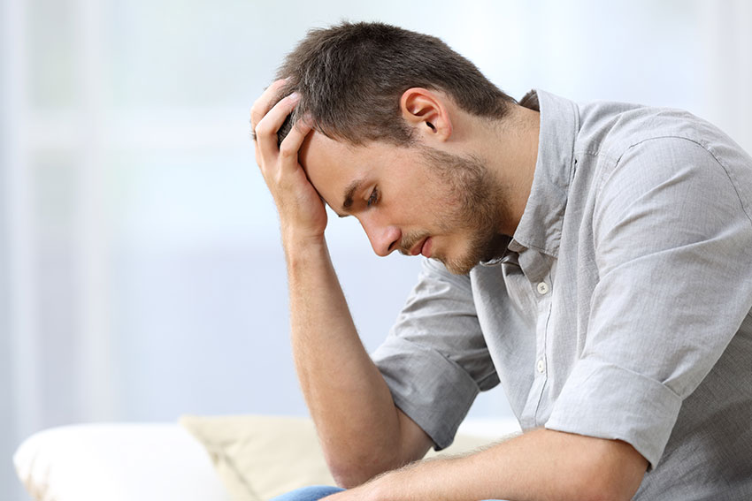 How-to-Avoid-a-Case-of-Dental-Regret sad young man sits on the edge of his bed, disappointed.