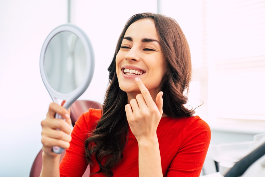 woman inspecting her smile with new dental implants after recovering from surgery 